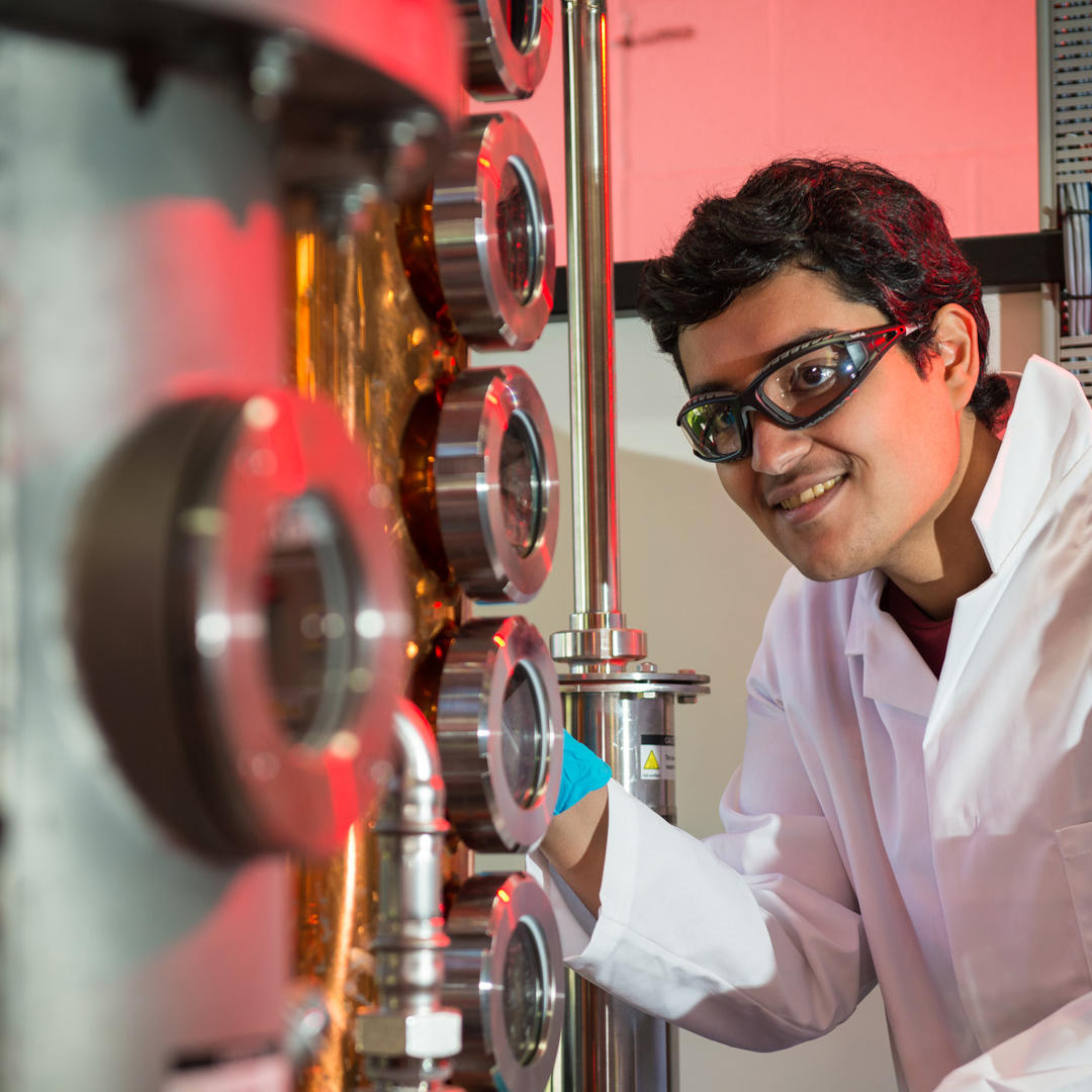 A Chemical Engineering student in a white coat and protective gloves using equipment in a lab 