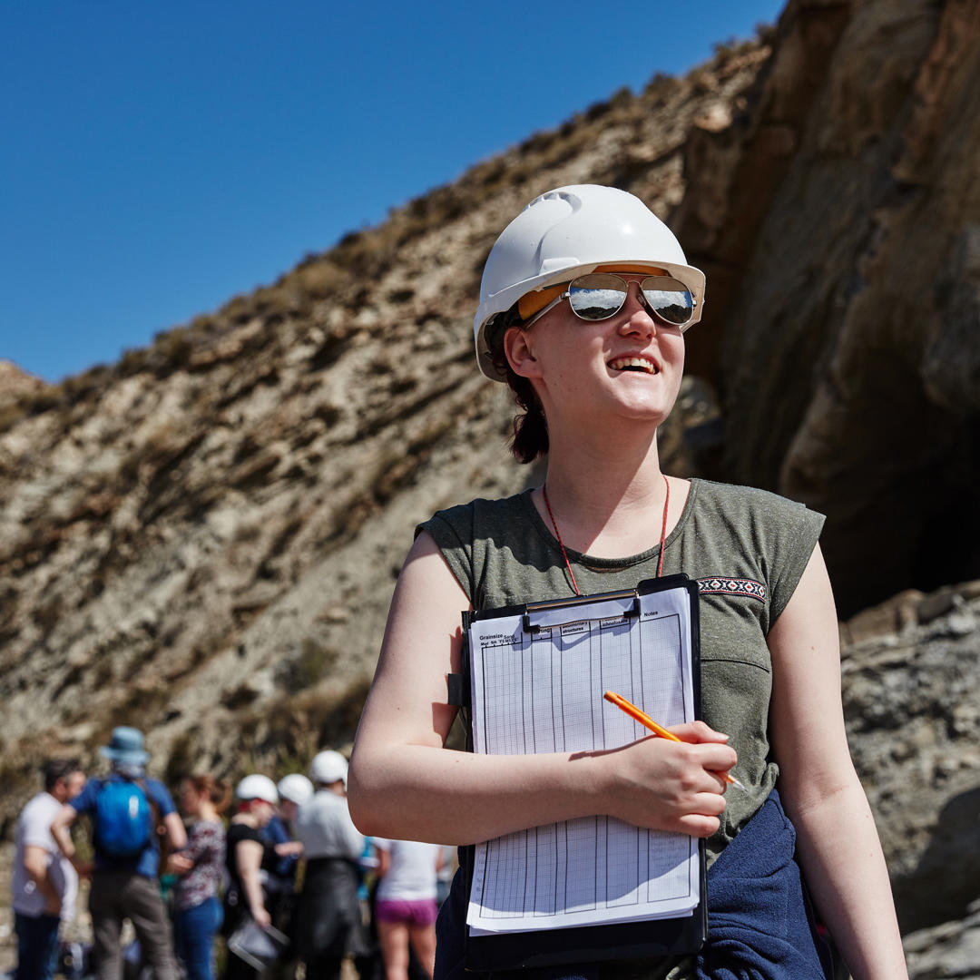 A female Geology student wears a hard hat and holds a clipboard on a Field Trip in Spain