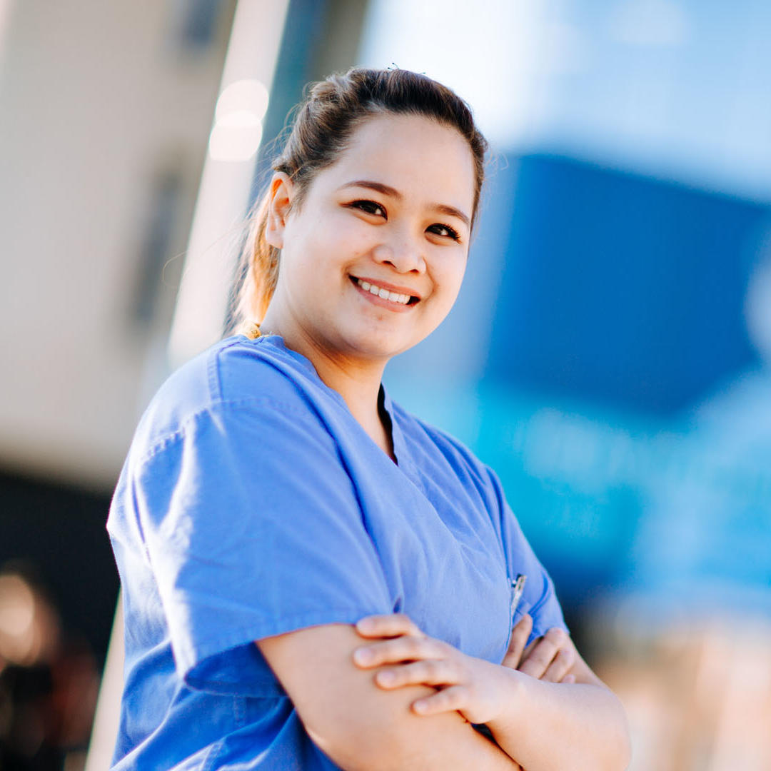 A medical student in blue scrubs outside the Allam Medical Building