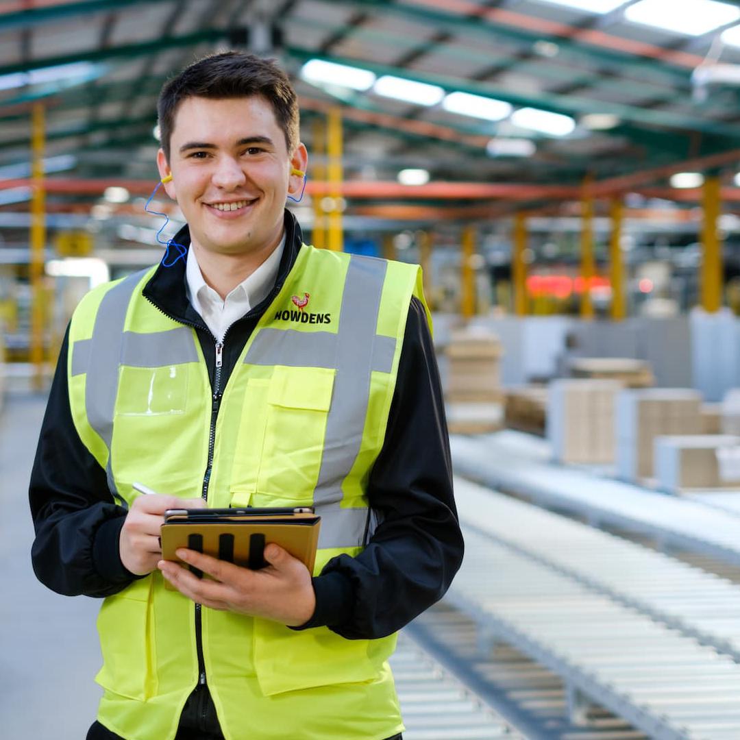 An Mechanical Engineering Intern in a high vis vest standing in a manufacturing warehouse 