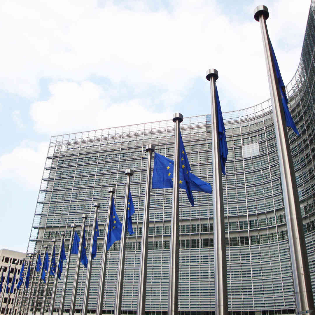 An external photo of the European Union headquarters in Brussels with three EU flags flying at the front