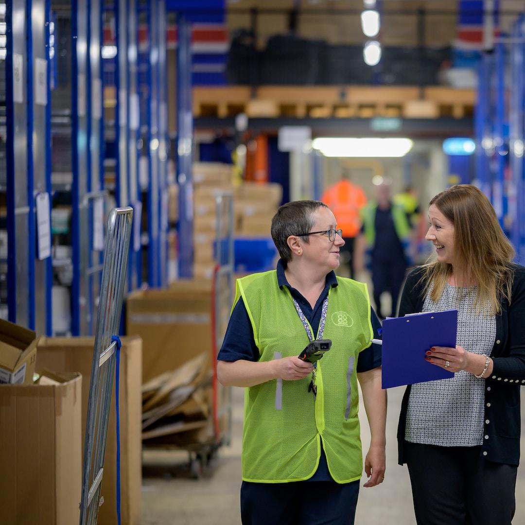 Two factory workers in hi vis vests walking with a clipboard