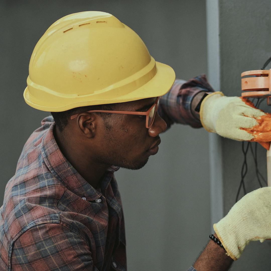 An electrician in a hard hat and protective gloves working on a home circuit
