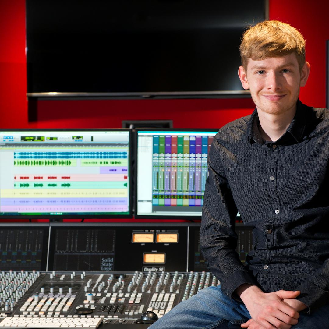 A male music student sat on a desk in a studio